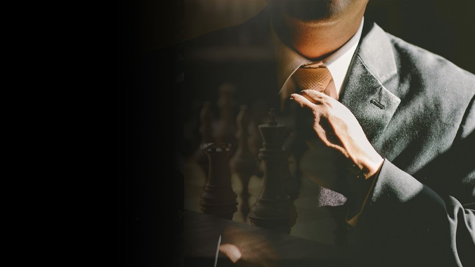 A man in a dark suit adjusting his tie over a chessboard